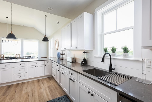 kitchen with light wood-style flooring, a sink, visible vents, hanging light fixtures, and dark countertops