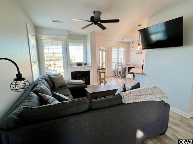 living area featuring baseboards, visible vents, a ceiling fan, a glass covered fireplace, and light wood-style floors