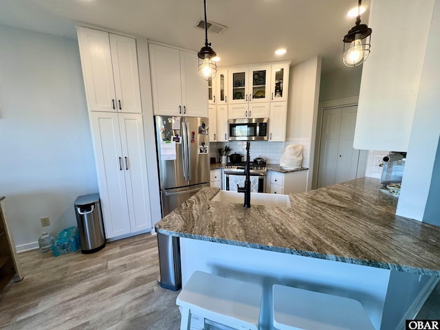 kitchen featuring decorative backsplash, appliances with stainless steel finishes, white cabinetry, dark stone countertops, and a peninsula