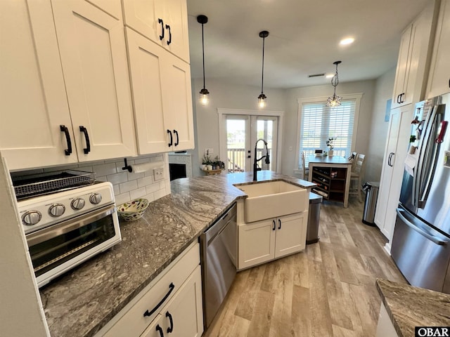 kitchen featuring light wood finished floors, decorative backsplash, dark stone countertops, stainless steel appliances, and a sink