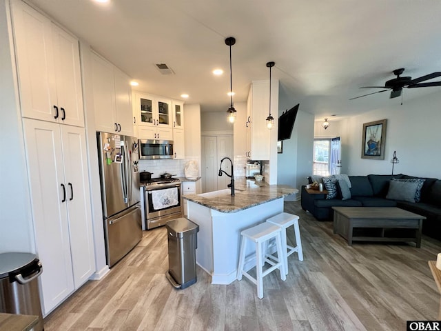 kitchen featuring stainless steel appliances, a breakfast bar, a peninsula, a sink, and white cabinetry