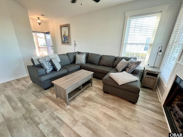 living area with plenty of natural light, a fireplace, a ceiling fan, and light wood-style floors