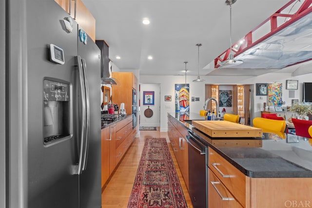 kitchen featuring dark countertops, a large island, appliances with stainless steel finishes, pendant lighting, and a sink