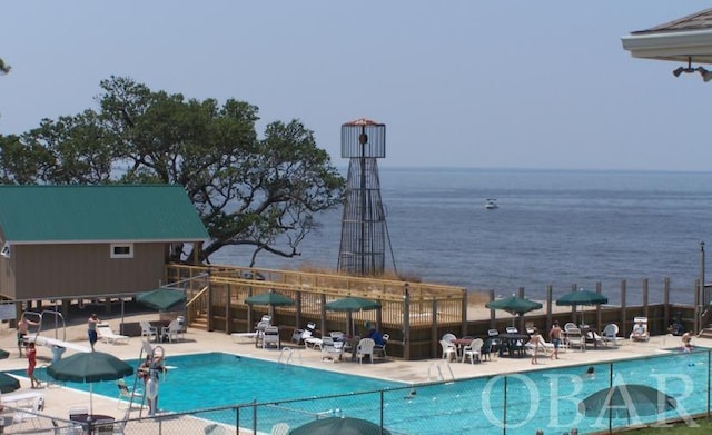 community pool featuring a patio area, a water view, and fence