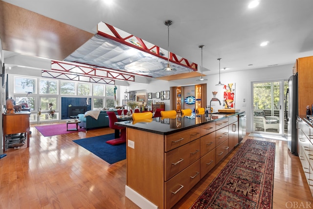 kitchen featuring brown cabinets, dark countertops, appliances with stainless steel finishes, open floor plan, and a kitchen island with sink