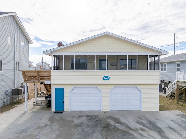 view of front of property featuring central AC unit, an attached garage, a sunroom, driveway, and a chimney