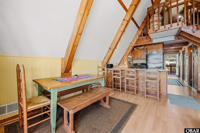 dining space featuring wood walls, vaulted ceiling with beams, and wood finished floors