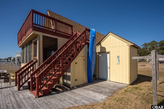 rear view of house with a shingled roof, stairs, a deck, an outdoor structure, and a storage unit