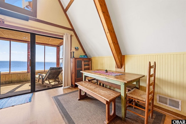 dining area with visible vents, a water view, a wainscoted wall, vaulted ceiling, and wood finished floors