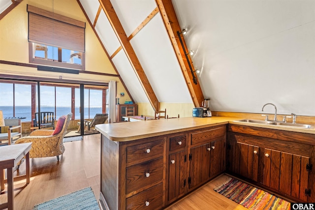 kitchen with lofted ceiling with beams, light wood-style flooring, a peninsula, a sink, and light countertops