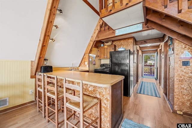 kitchen featuring wooden walls, a peninsula, black appliances, light wood-style floors, and wainscoting