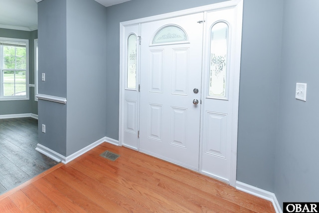 entrance foyer with visible vents, wood finished floors, baseboards, and ornamental molding