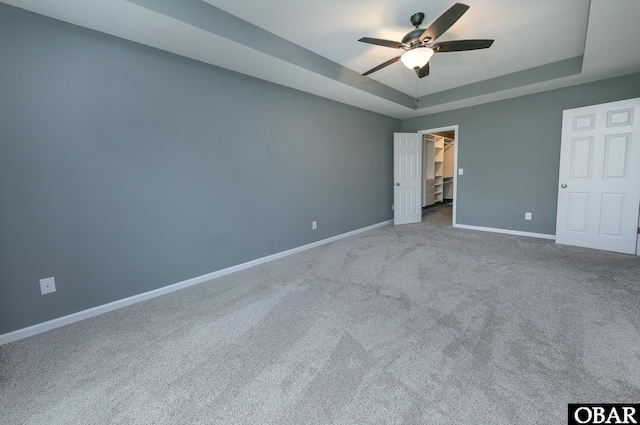 unfurnished bedroom with a ceiling fan, a spacious closet, carpet floors, a tray ceiling, and baseboards
