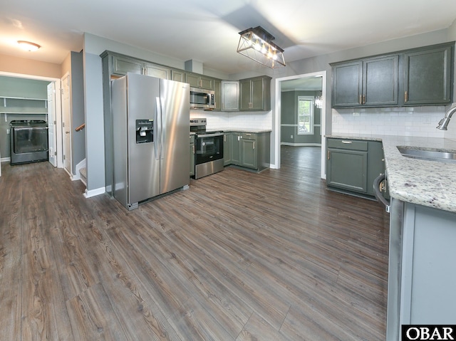 kitchen with dark wood-style floors, a sink, backsplash, washer / clothes dryer, and appliances with stainless steel finishes