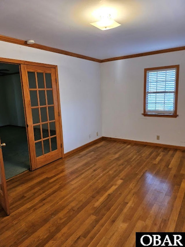 spare room featuring crown molding, baseboards, and wood finished floors