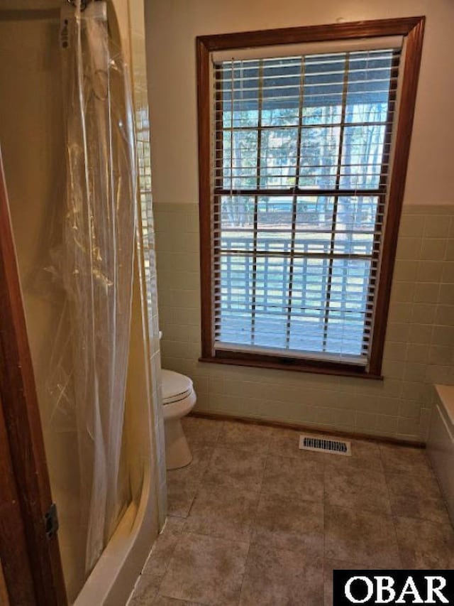 full bath featuring toilet, a shower with shower curtain, visible vents, and tile walls