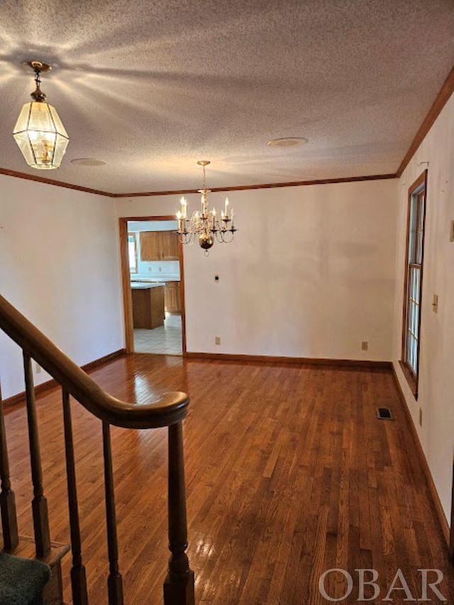 interior space featuring a textured ceiling, ornamental molding, wood finished floors, and visible vents