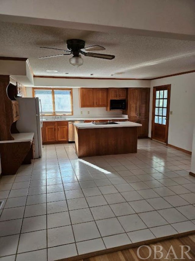 kitchen featuring a center island, light countertops, brown cabinetry, freestanding refrigerator, and black microwave