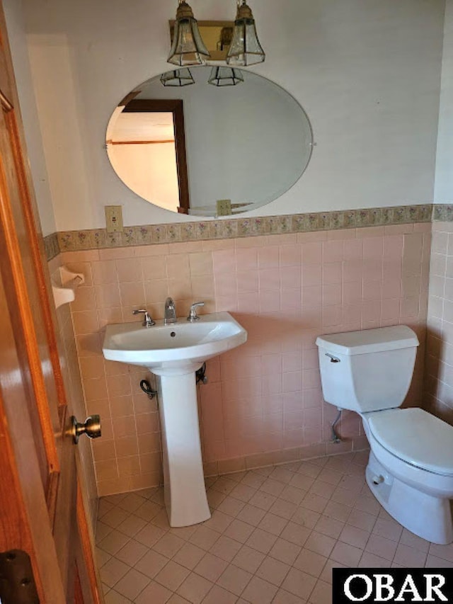 half bath with wainscoting, tile walls, toilet, and tile patterned floors