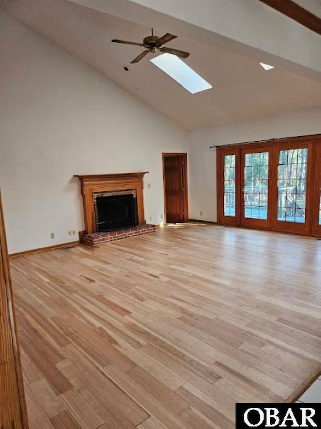 unfurnished living room with a skylight, a fireplace, light wood finished floors, a ceiling fan, and high vaulted ceiling