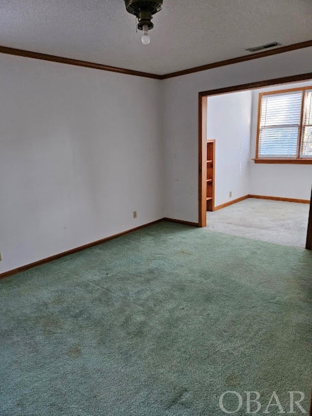 empty room with visible vents, baseboards, ornamental molding, carpet, and a textured ceiling