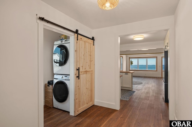 laundry area featuring a barn door, stacked washer / dryer, dark wood-style floors, and laundry area