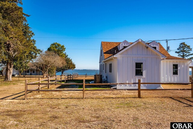 view of side of home with board and batten siding, a shingled roof, a water view, and fence