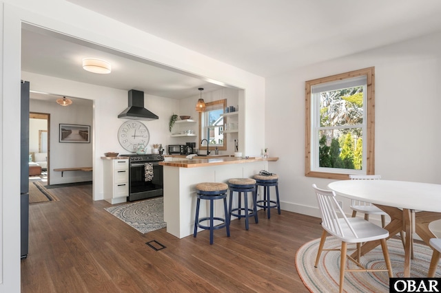 kitchen with dark wood-style flooring, electric range oven, black microwave, a kitchen bar, and wall chimney range hood