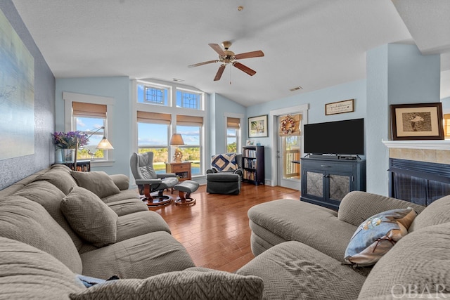 living room featuring lofted ceiling, a tile fireplace, wood finished floors, a ceiling fan, and baseboards