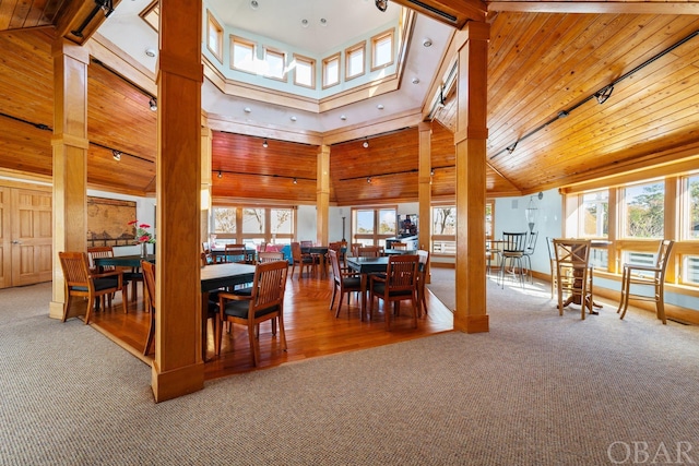 carpeted dining space with high vaulted ceiling, wooden ceiling, decorative columns, and beamed ceiling