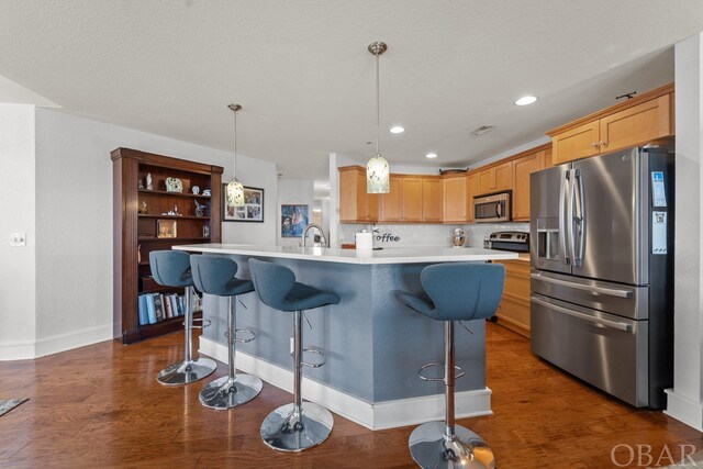 kitchen with stainless steel appliances, a kitchen breakfast bar, light countertops, an island with sink, and decorative light fixtures