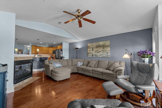 living area with a fireplace, a ceiling fan, vaulted ceiling, and dark wood-type flooring