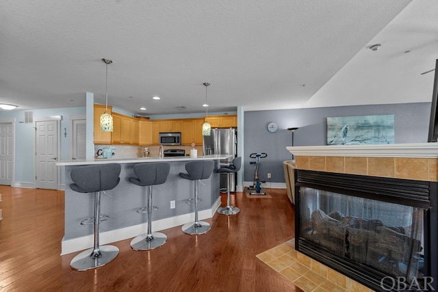 kitchen featuring stainless steel appliances, light countertops, light brown cabinetry, a kitchen bar, and pendant lighting