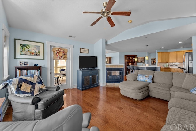 living area featuring light wood finished floors, lofted ceiling, visible vents, a ceiling fan, and a tile fireplace