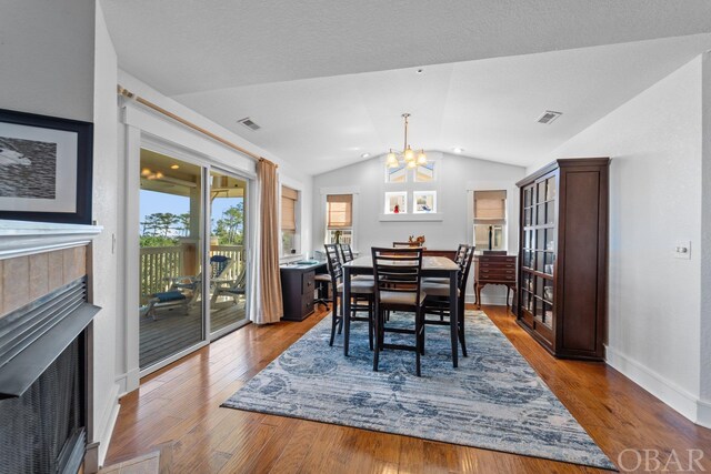 dining space with a notable chandelier, visible vents, vaulted ceiling, light wood finished floors, and a tiled fireplace