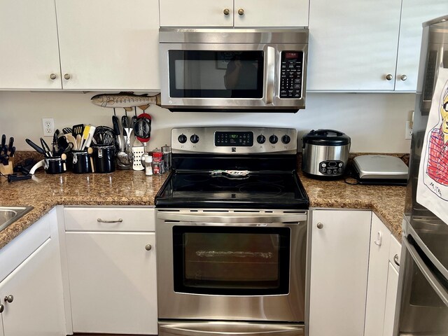 kitchen with dark stone counters, appliances with stainless steel finishes, and white cabinets