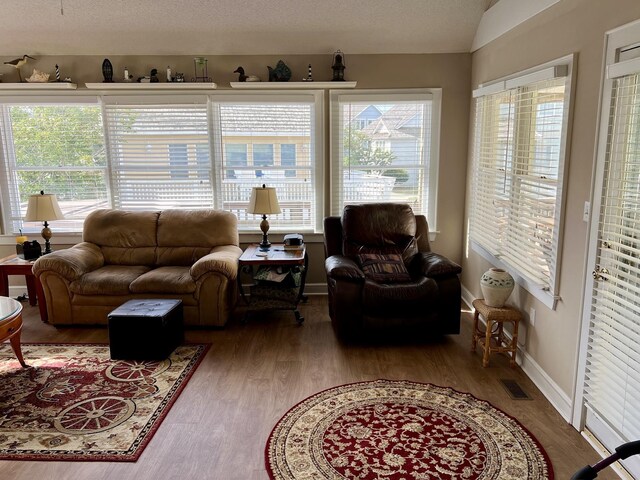 living area with baseboards, visible vents, vaulted ceiling, and wood finished floors