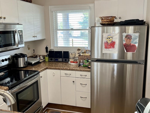 kitchen with stainless steel appliances, dark stone counters, and white cabinets