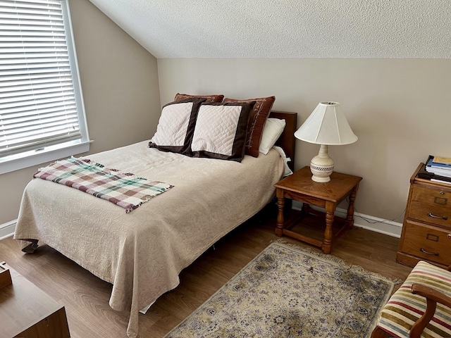 bedroom with dark wood-style floors, a textured ceiling, lofted ceiling, and baseboards