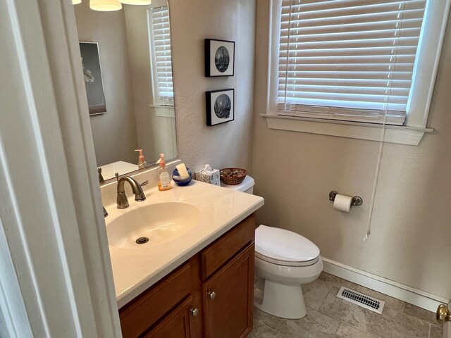 half bathroom featuring toilet, vanity, visible vents, and baseboards