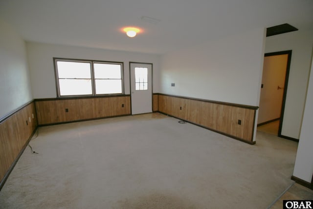 unfurnished room featuring light colored carpet, wainscoting, and wooden walls