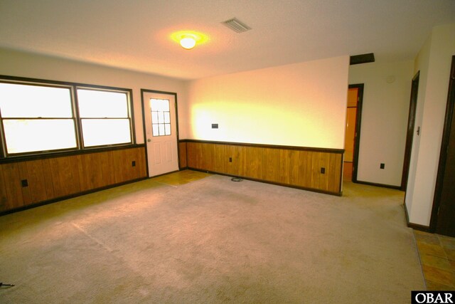 unfurnished room featuring wood walls, visible vents, light colored carpet, and wainscoting