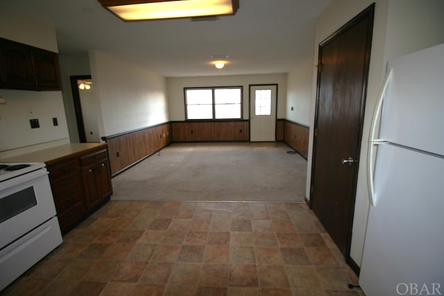 kitchen with wooden walls, light carpet, white appliances, light countertops, and wainscoting