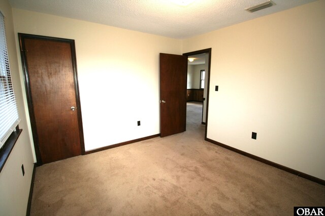 unfurnished bedroom with baseboards, visible vents, light carpet, and a textured ceiling