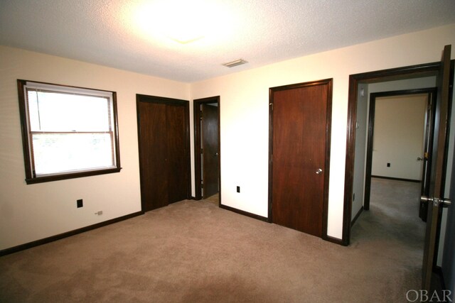 unfurnished bedroom with baseboards, visible vents, a textured ceiling, carpet floors, and multiple closets