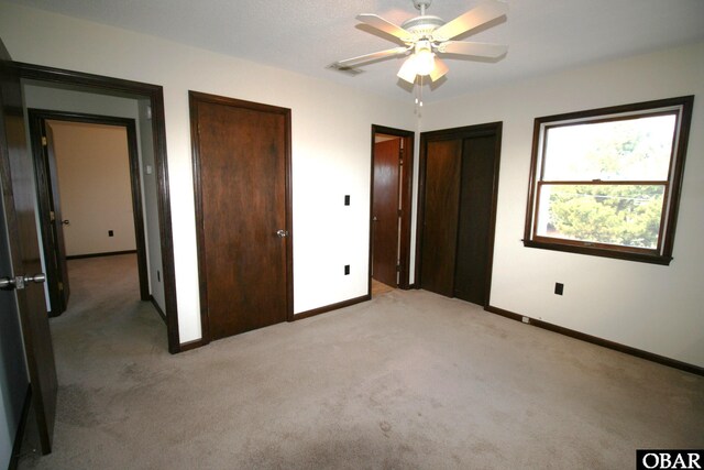 unfurnished bedroom with light carpet, baseboards, visible vents, and multiple closets