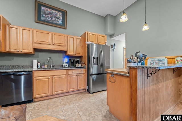 kitchen featuring light stone counters, pendant lighting, a high ceiling, appliances with stainless steel finishes, and a sink