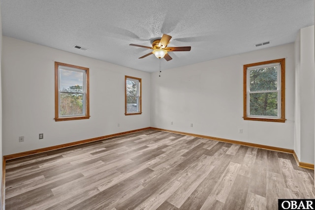 spare room with light wood-style floors, visible vents, a textured ceiling, and baseboards