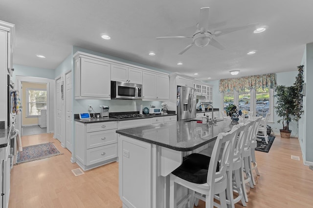 kitchen featuring stainless steel appliances, an island with sink, a sink, and white cabinets