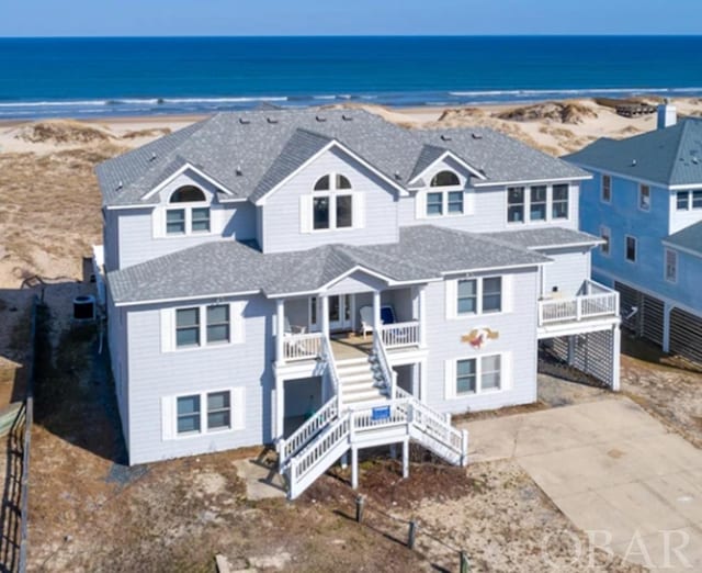 beach home with roof with shingles, a water view, covered porch, stairs, and a view of the beach